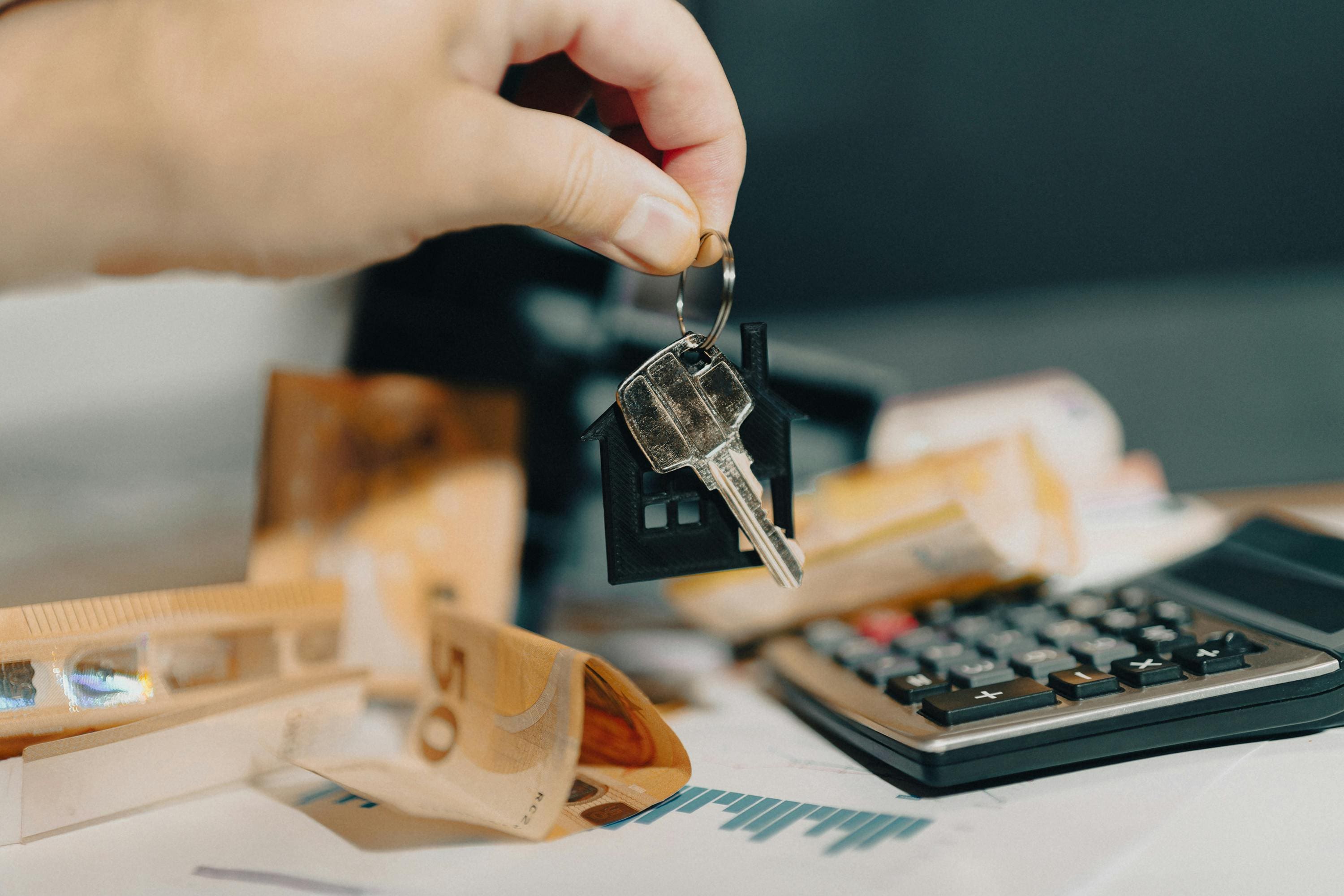 Hand holding keys over a calculator and money on a desk.