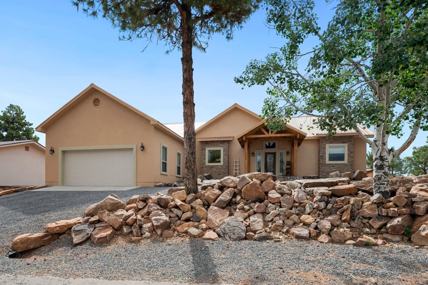 Single-story house with stone landscaping and a tall pine tree.
