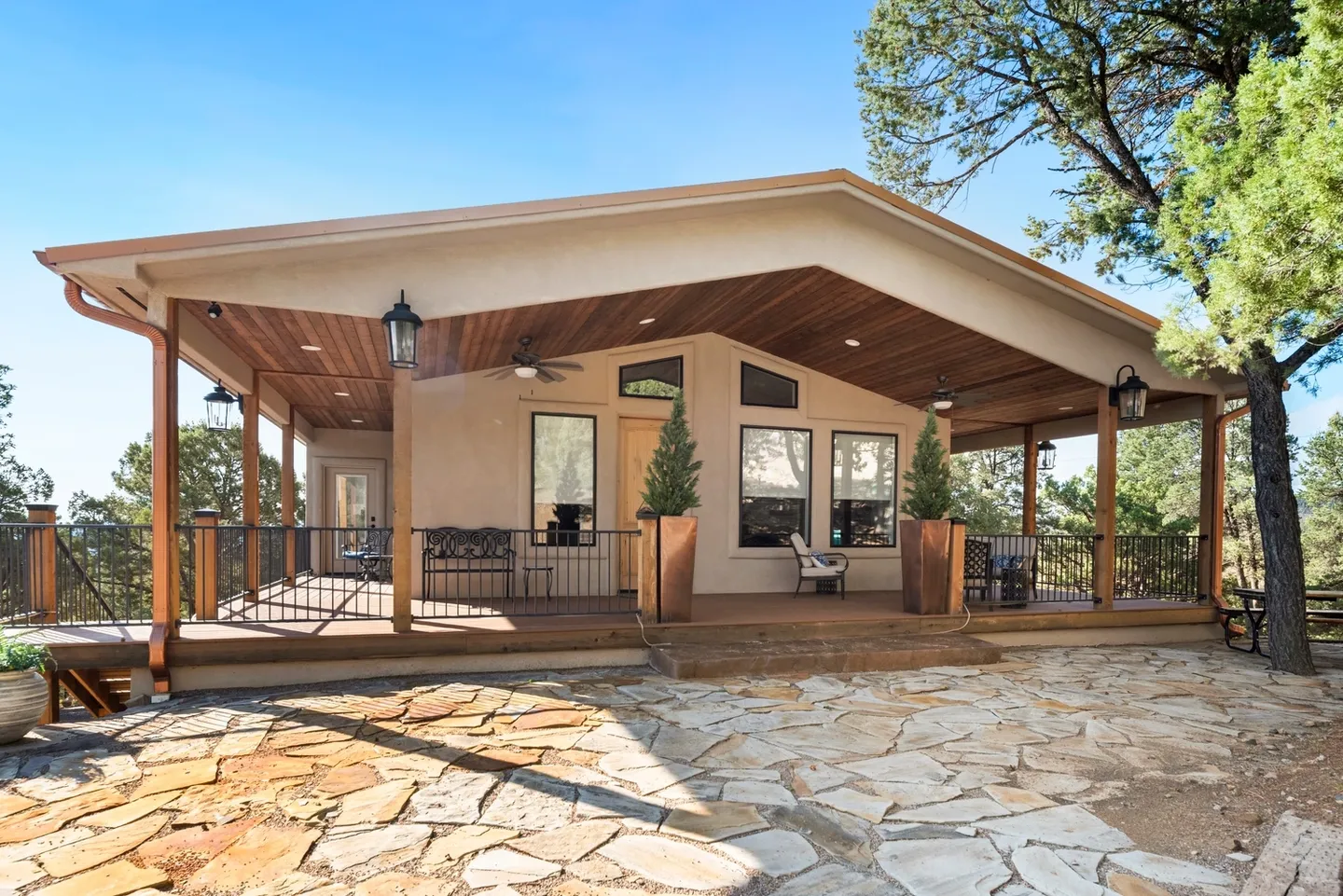 Cozy house with a spacious wooden porch and stone-paved yard under a clear blue sky.