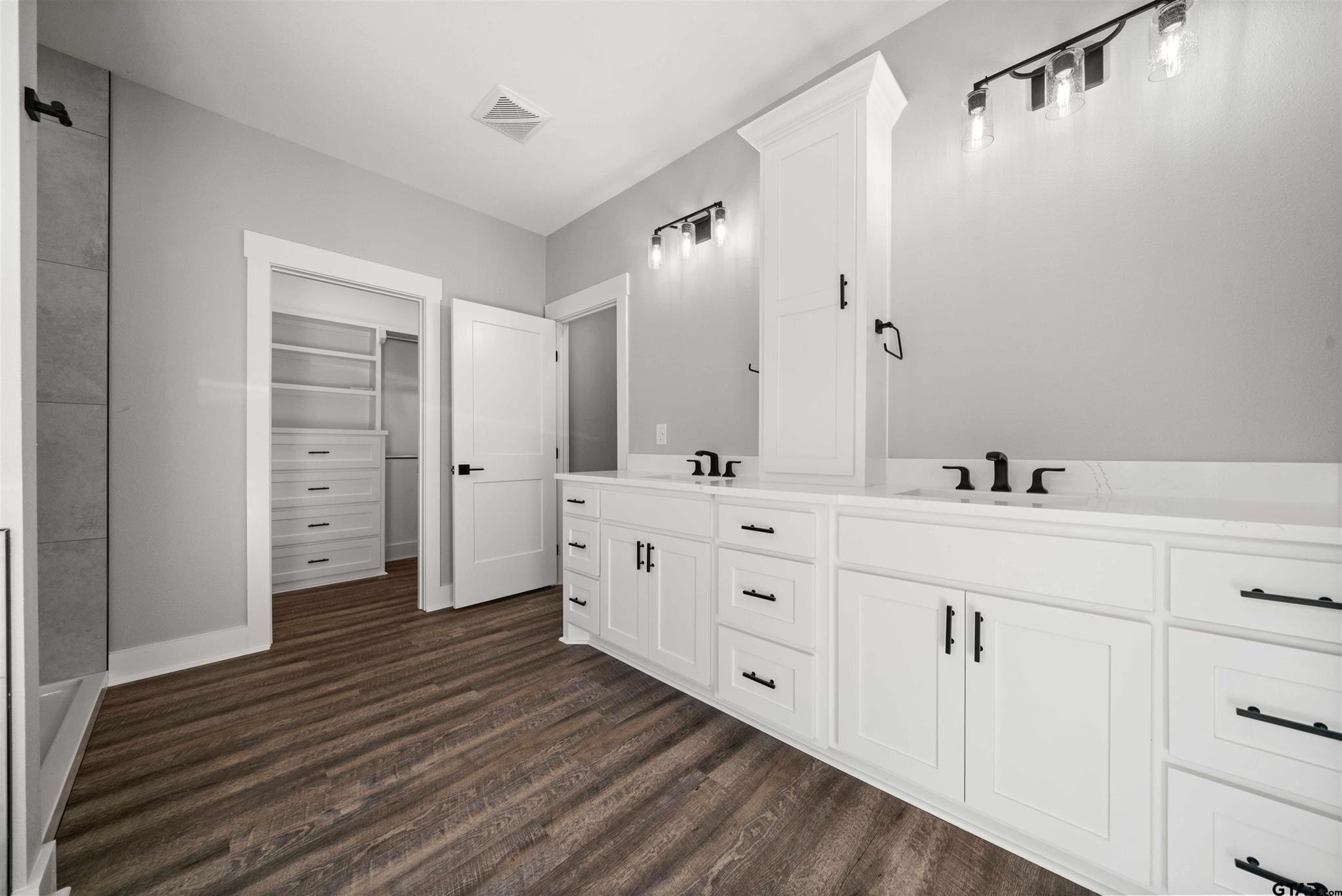 Spacious modern bathroom with white cabinetry and dark wood flooring.