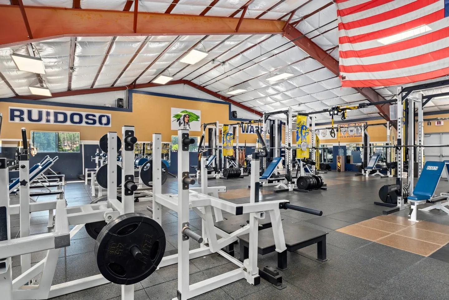 Spacious gym with various weightlifting and exercise equipment under a high ceiling.