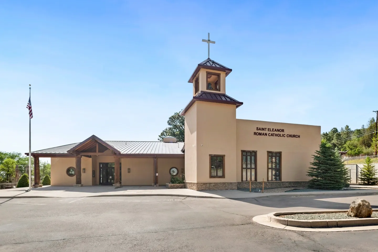 Front view of a beige church building with a cross on top under a clear blue sky.