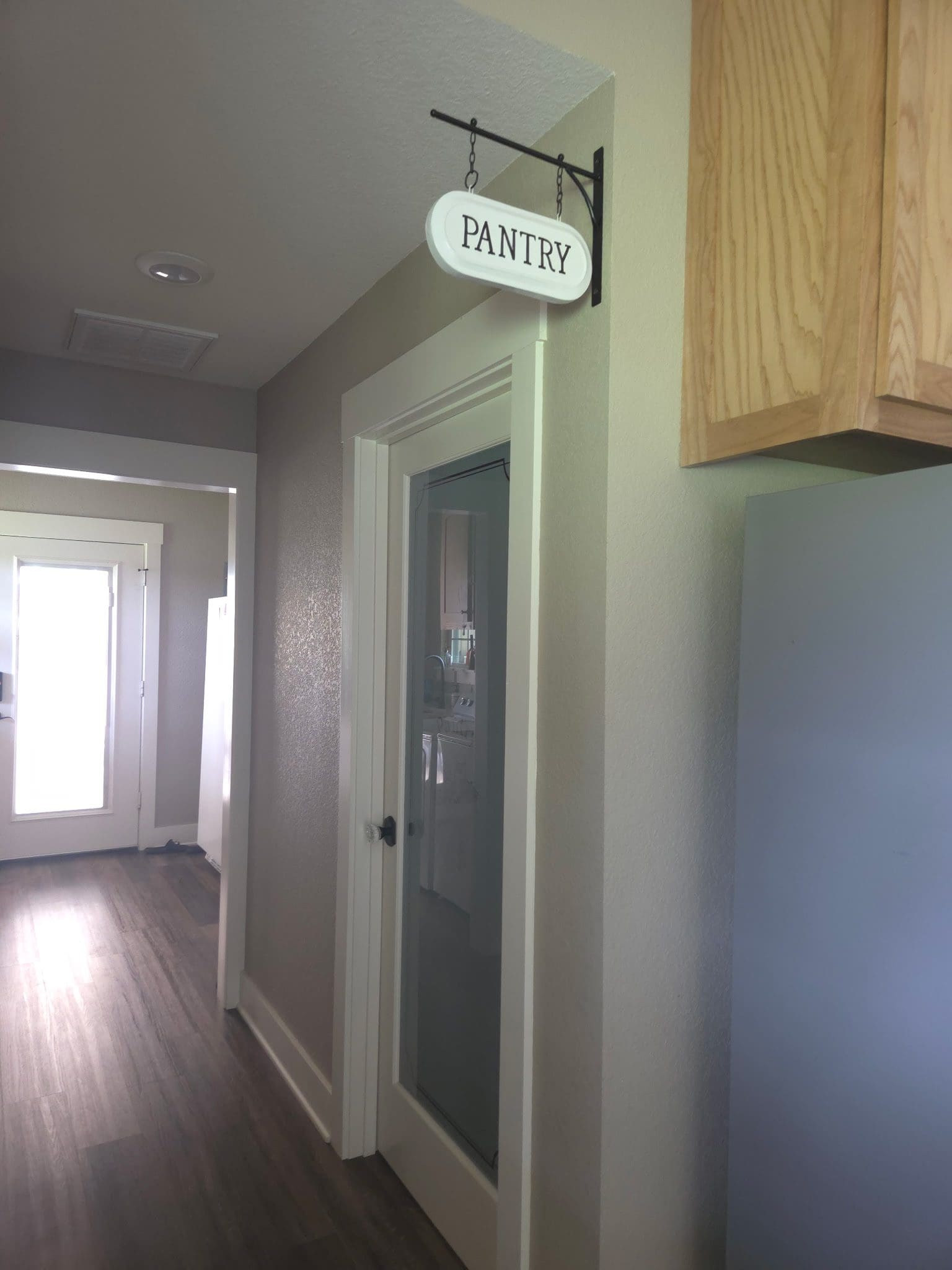 A hallway with a pantry door and wooden cabinets.