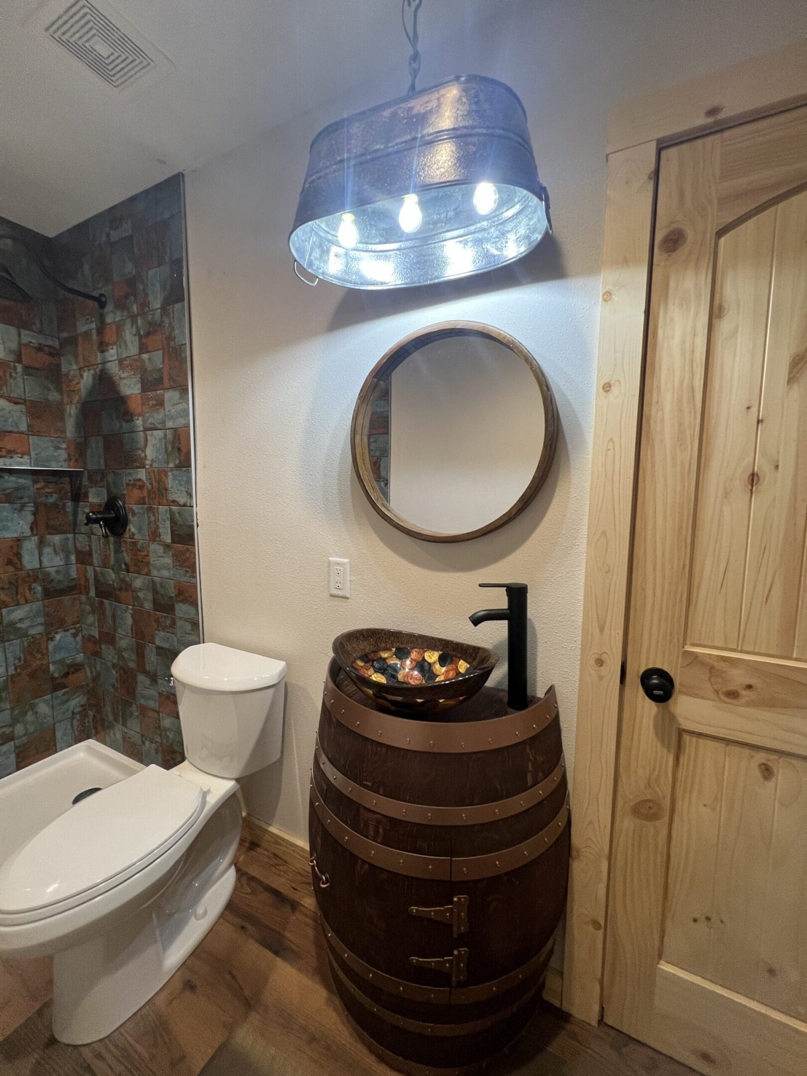 Rustic bathroom with barrel sink and round mirror.