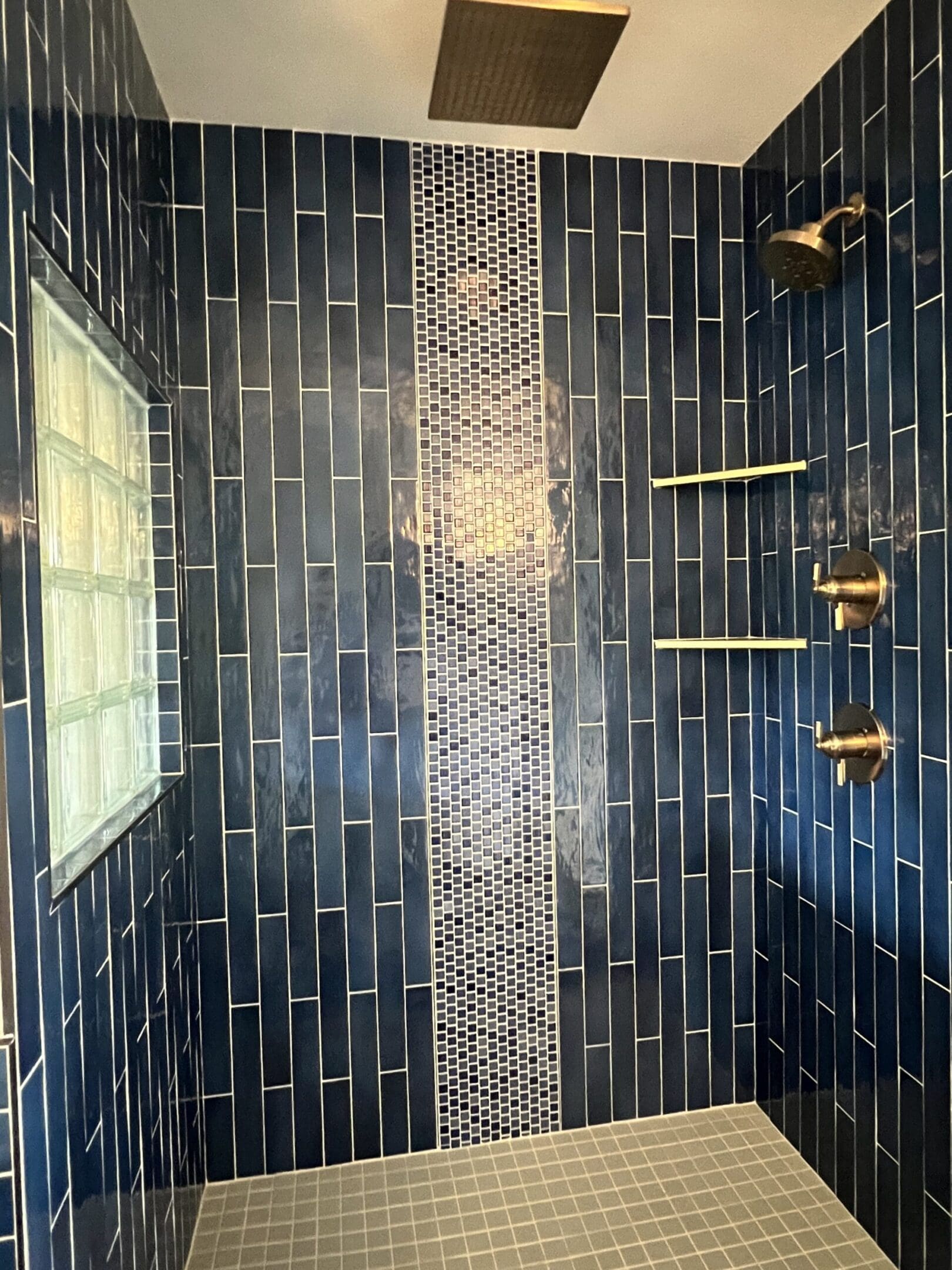 Modern shower with dark tiles and gold fixtures.