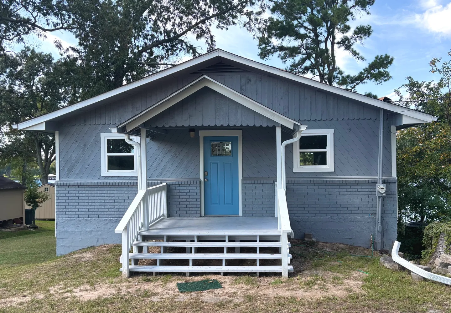 Gray house with blue door and white porch railing surrounded by trees.