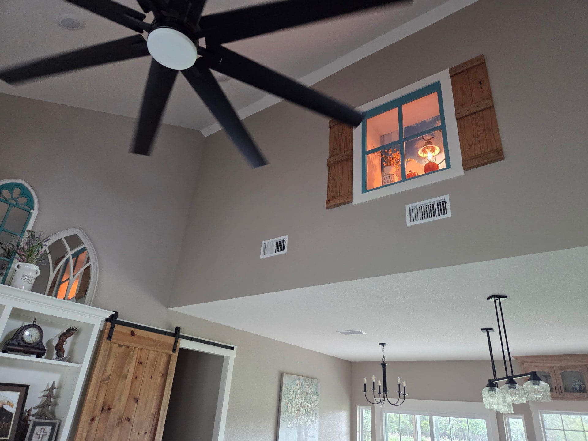 Ceiling fan with black blades in a modern room with a window showing a sunset.