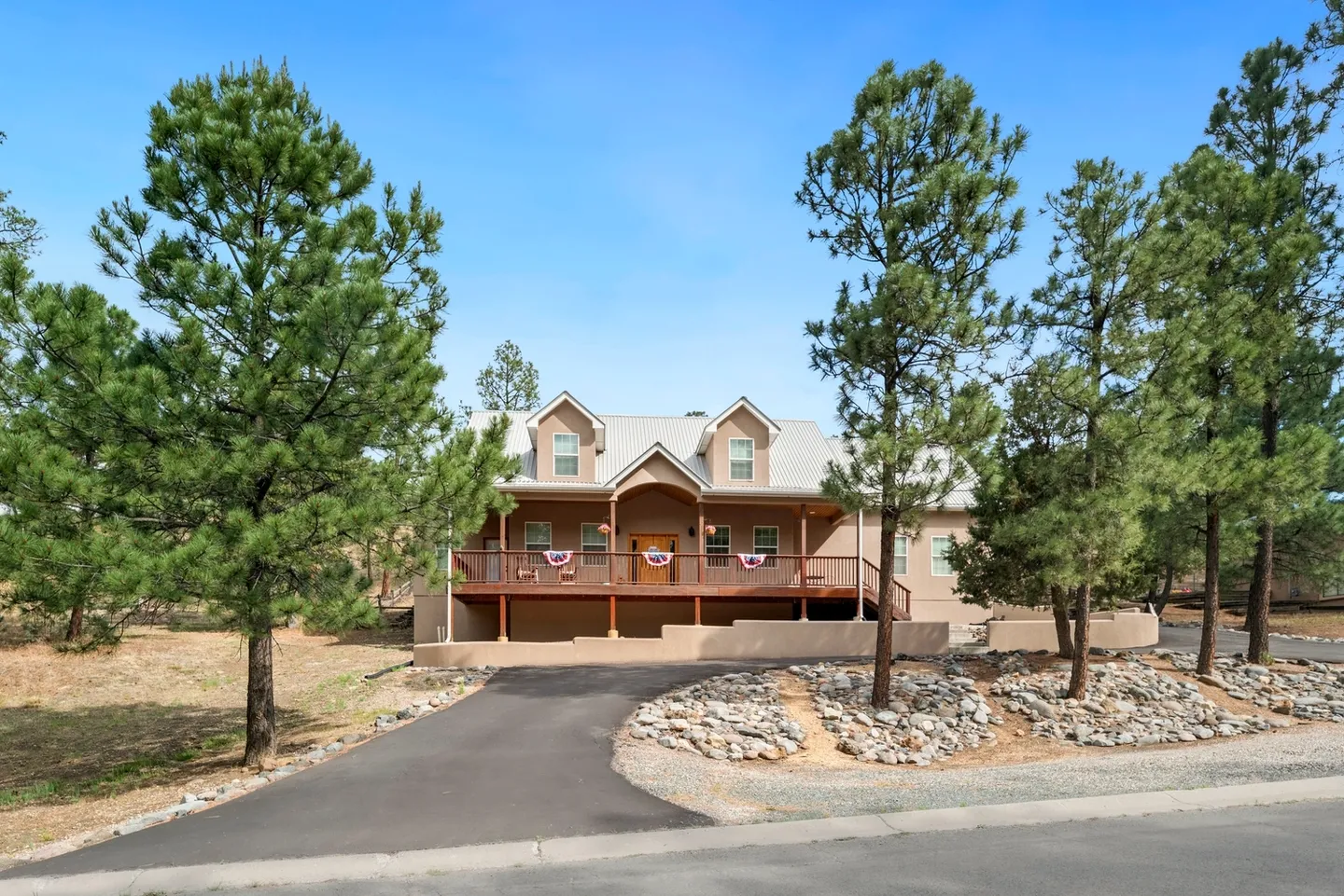 Spacious wooden house with a wraparound porch set among tall pine trees.