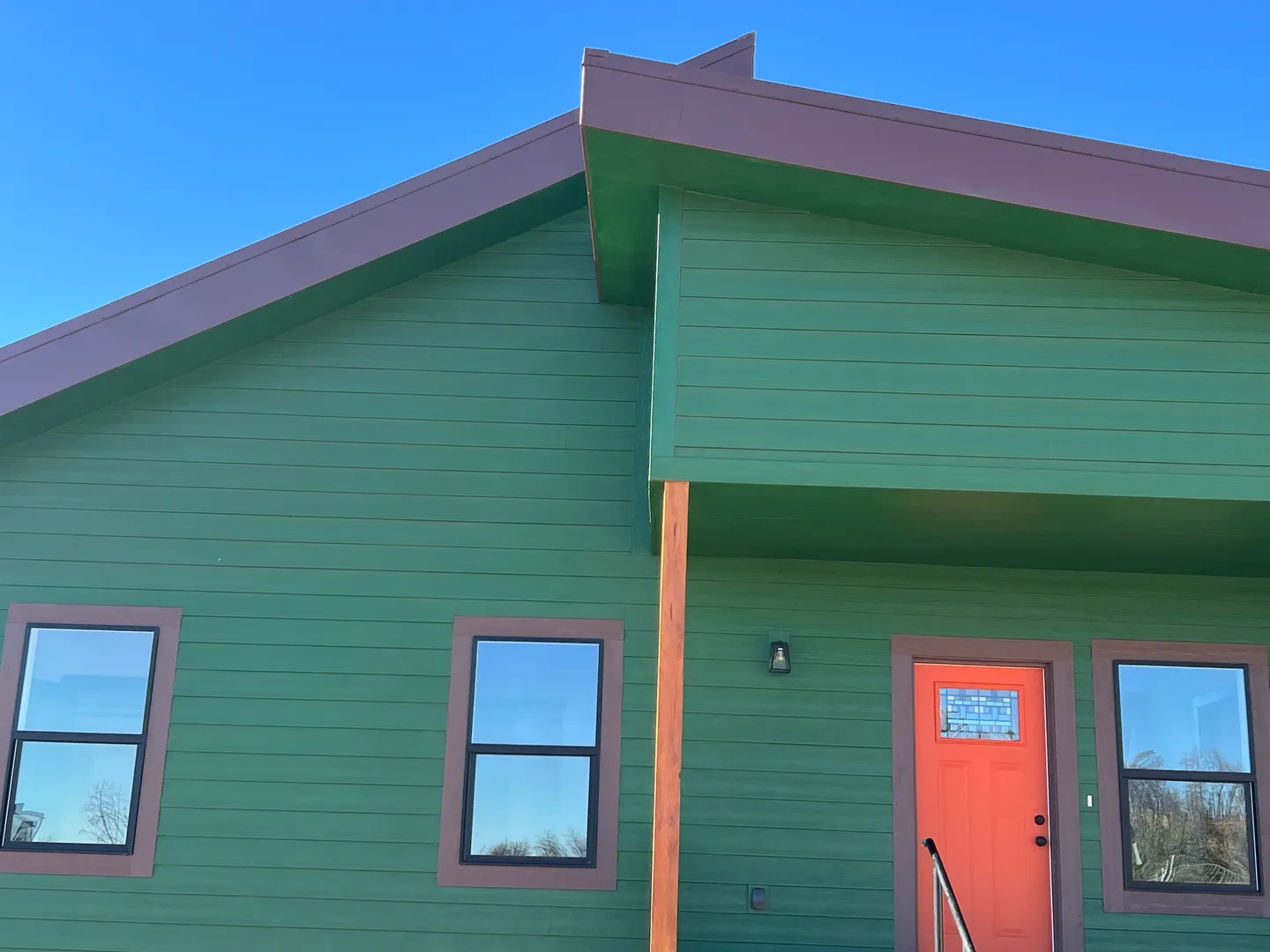 Green house with purple trim and a red door under a clear sky.