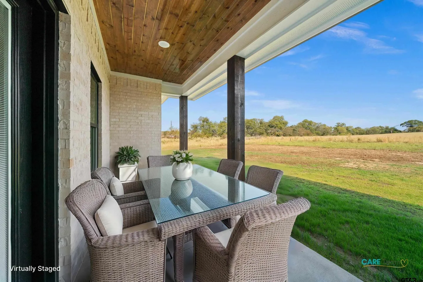 Outdoor dining area with wicker chairs and glass table overlooking a green field.