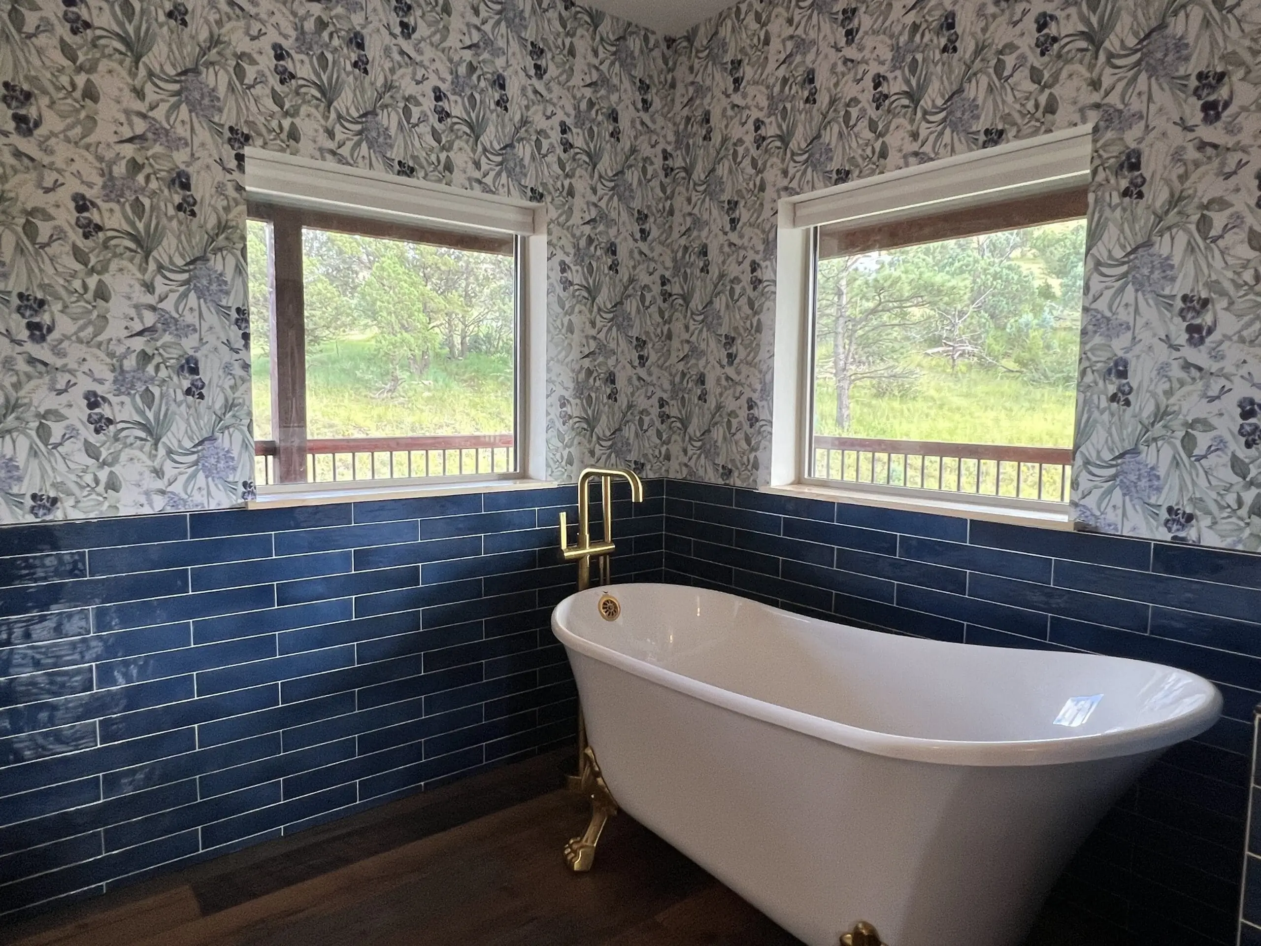 Elegant clawfoot bathtub in a floral and navy-tiled bathroom corner.
