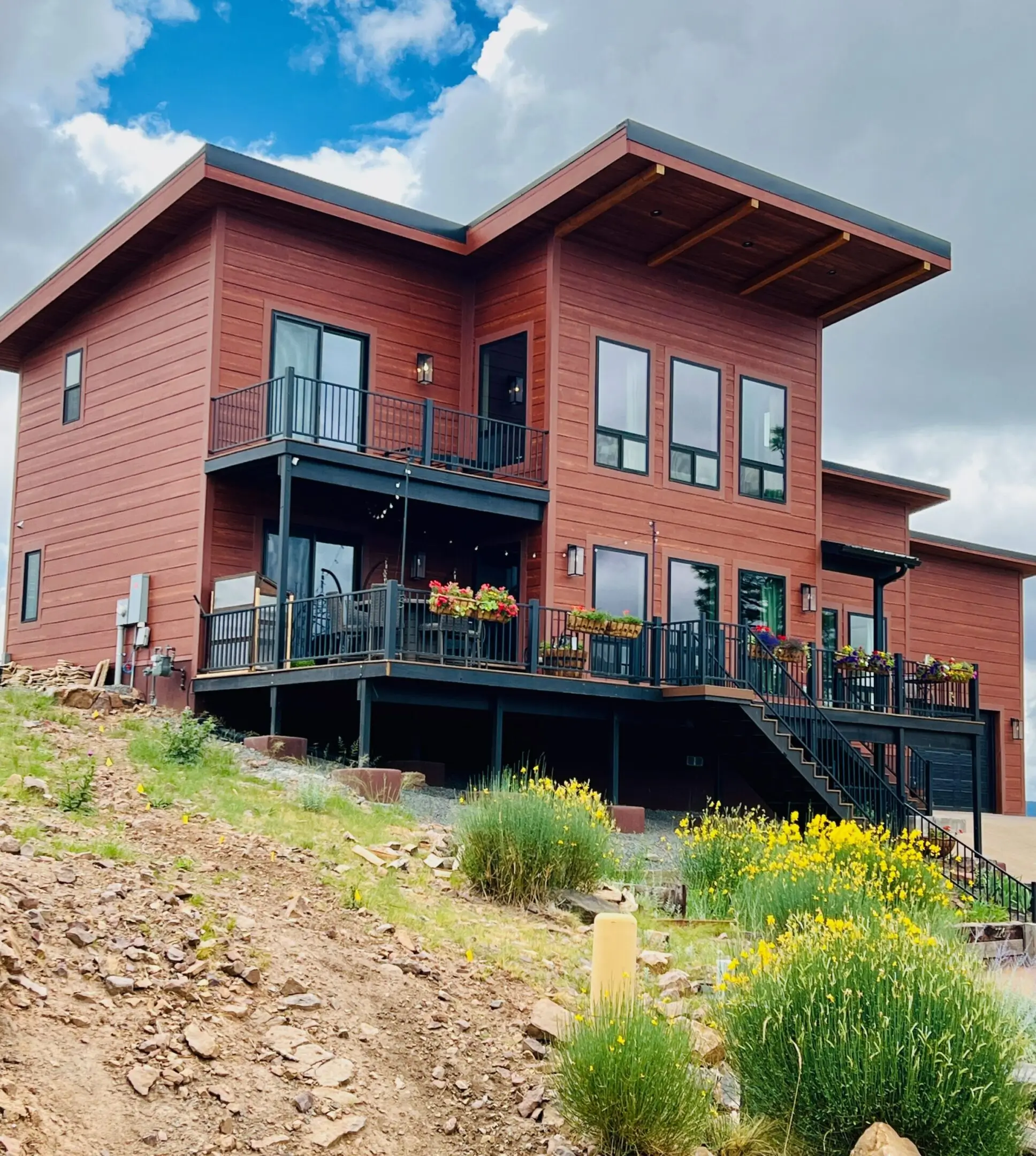 Modern two-story house with large windows and a balcony under a blue sky.